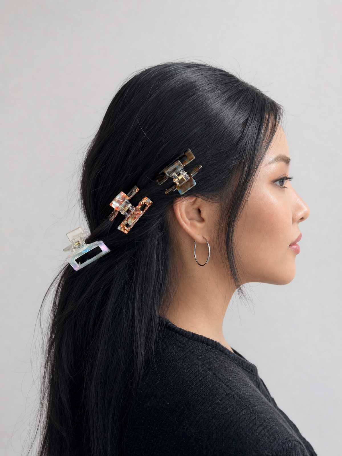 A woman with long black hair wearing three decorative claw hair clips in a glossy tortoiseshell pattern