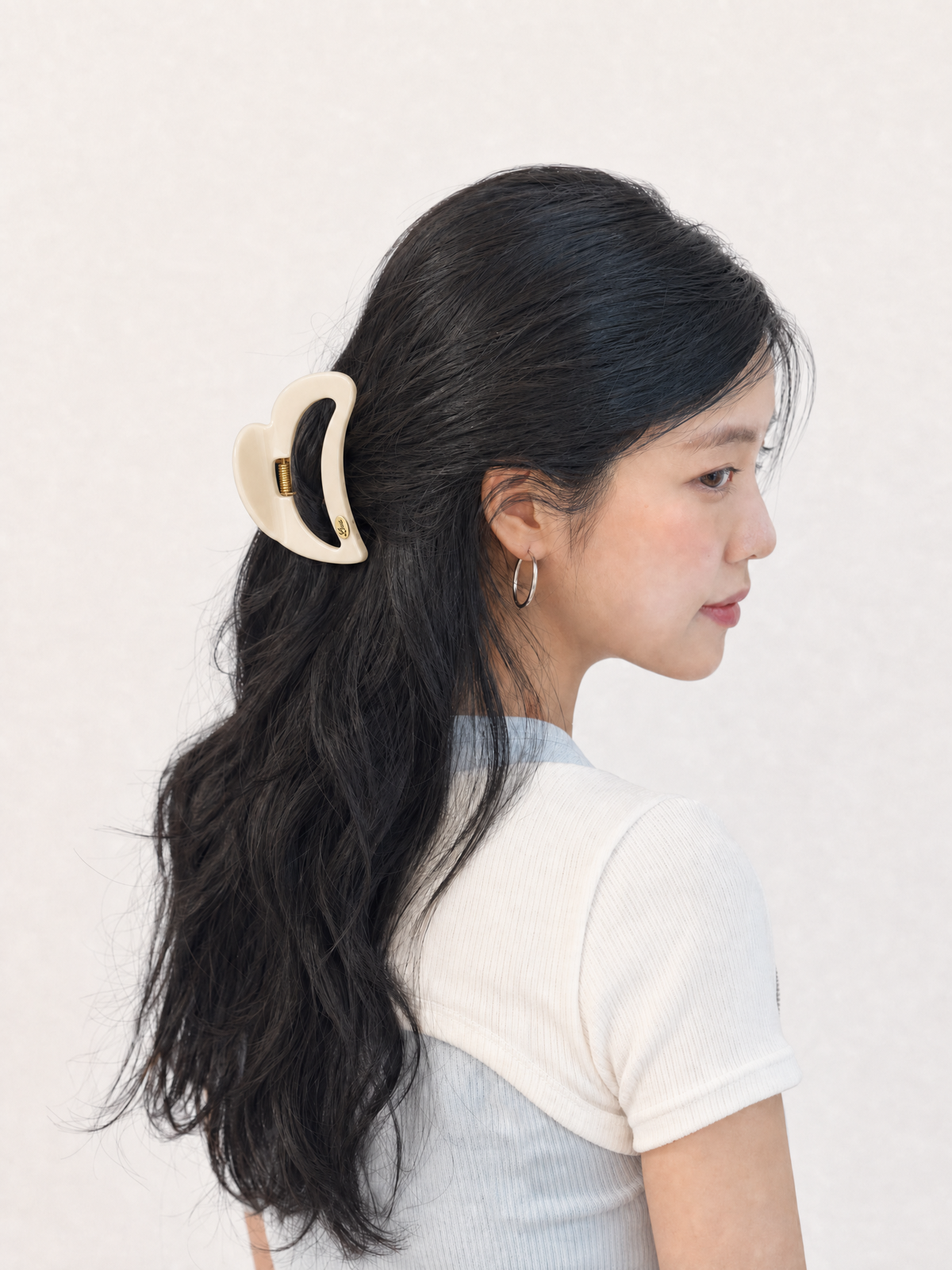 Side profile of model styling long hair with a soft buttermilk yellow heart-shaped claw clip