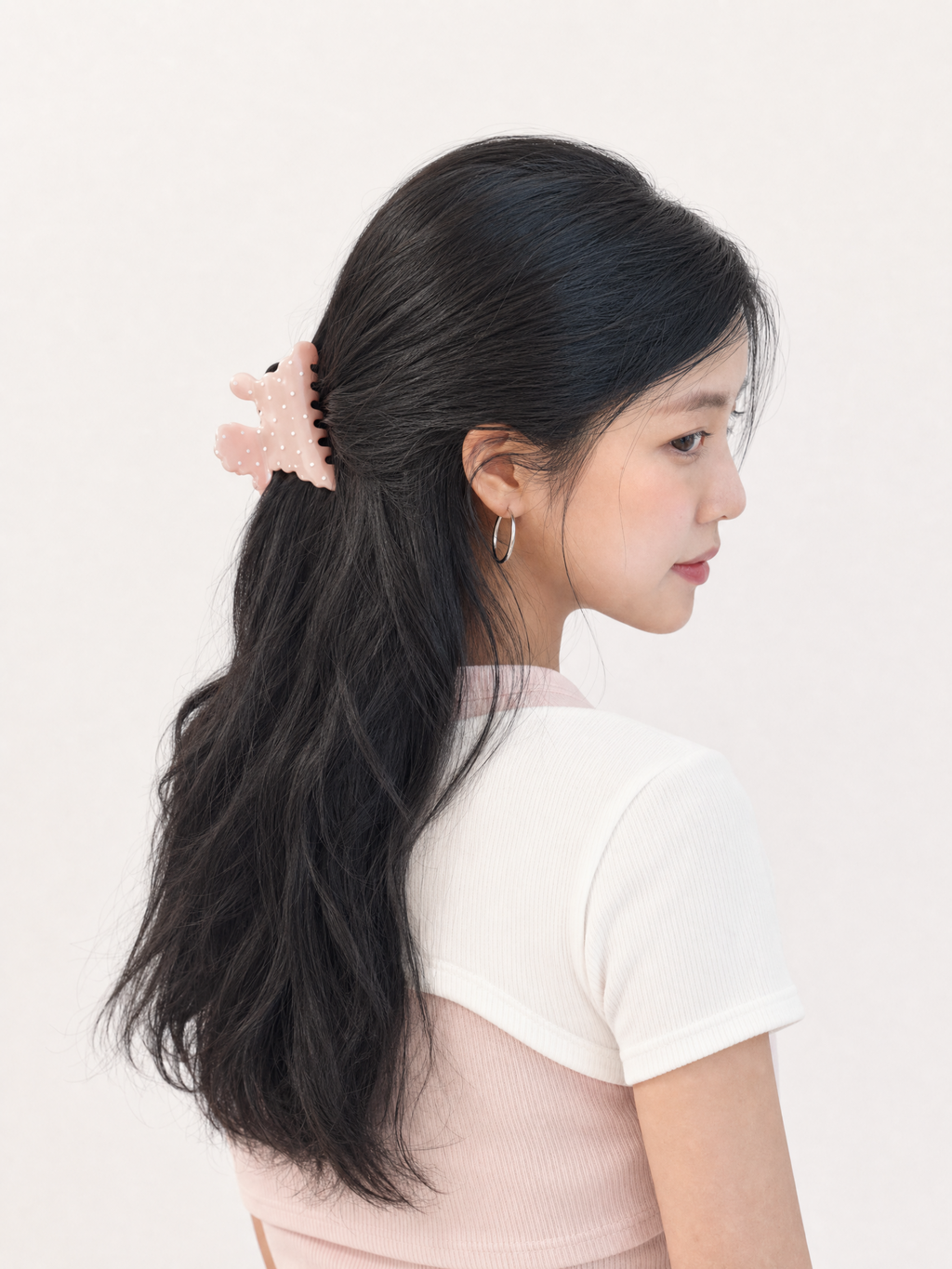 Model securing front face-framing pieces with a small dusty rose puppy polka dot hair clip for a playful Y2K look