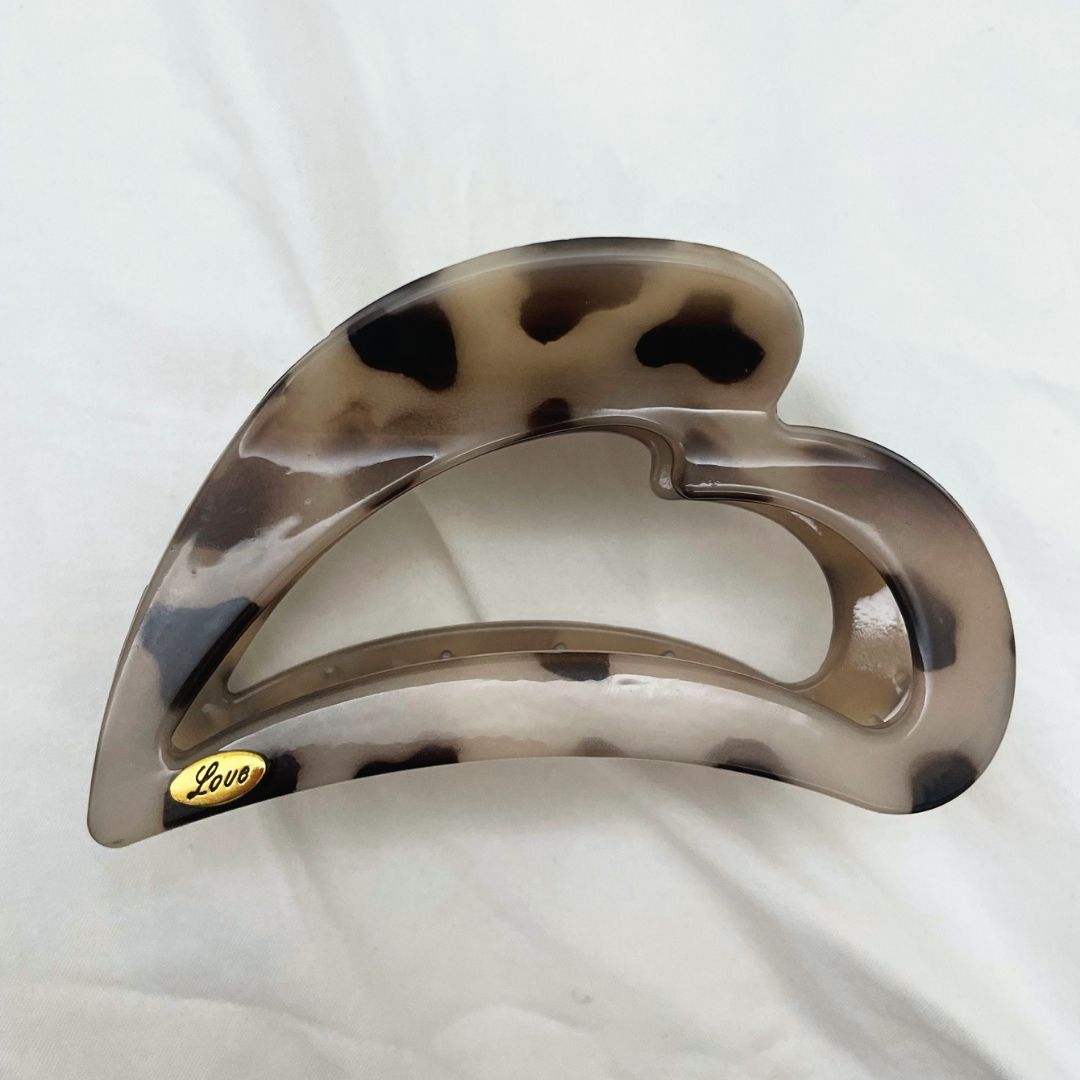 A tortoiseshell hair claw clip with a brown, beige, and black mottled pattern, featuring a small gold metal brand logo that reads 'Love'. 